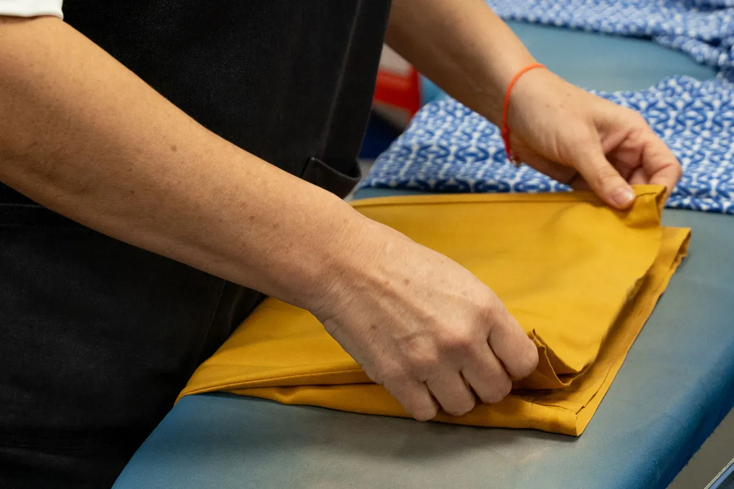 Hands folding a finished garment on a finishing table.