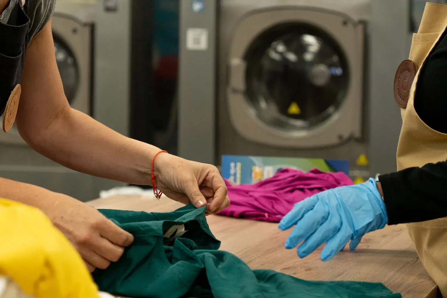 Gloved hands sorting and grading returned garments beside washing machines.